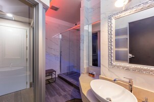 Een moderne badkamer met een glazen douchecabine, een ruim wastafelmeubel met een witte wastafel en een spiegel met een sierlijk omlijsting.