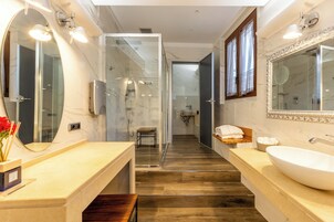 Un baño moderno con un espejo grande, dos lavamanos, una ducha y un mueble de tocador con un banco de madera.