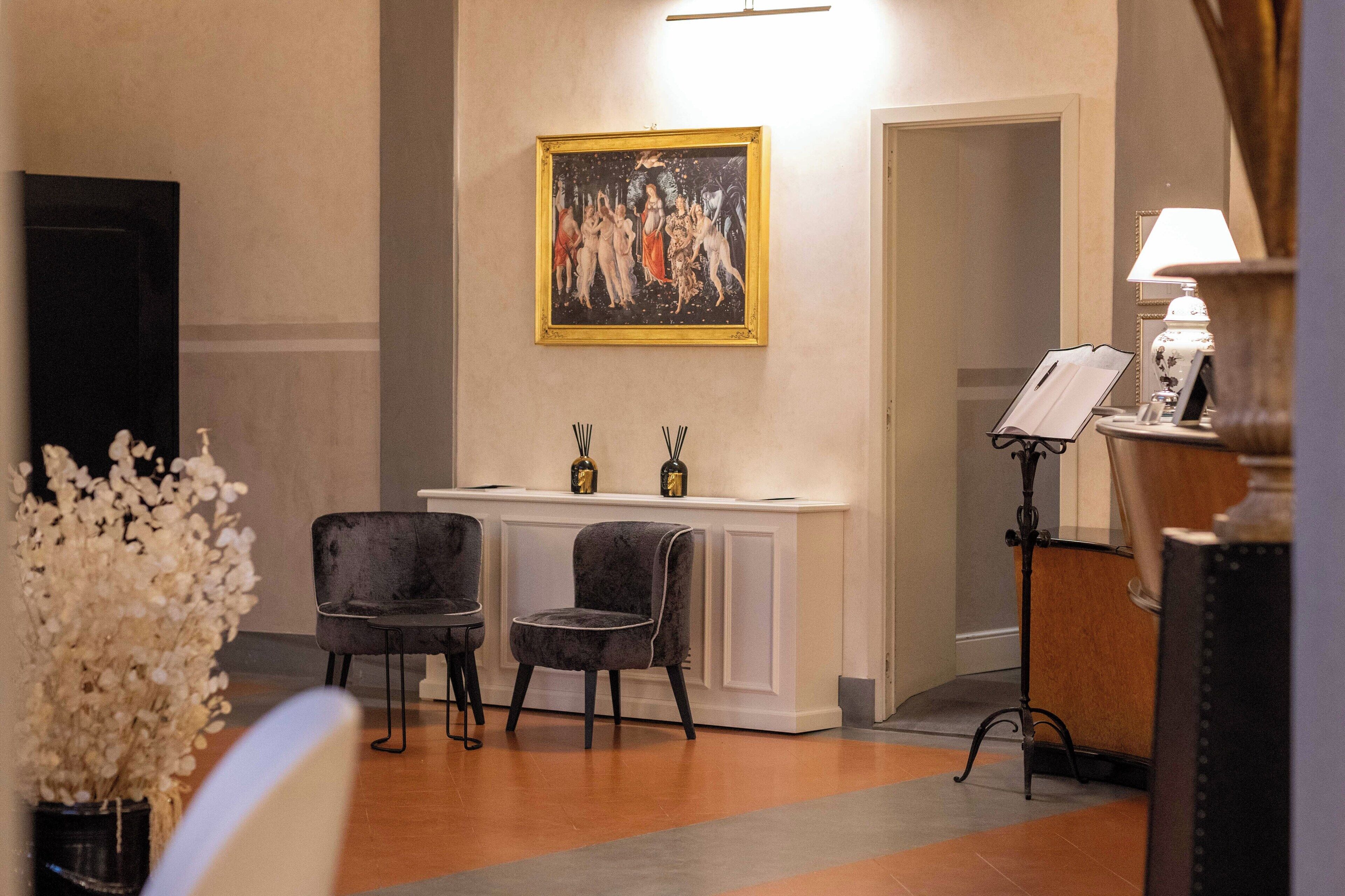 A lobby with a reception desk, two armchairs, a painting on the wall, and a lamp on a side table.