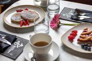 A dining table with plates of food, a cup of coffee, and cutlery.