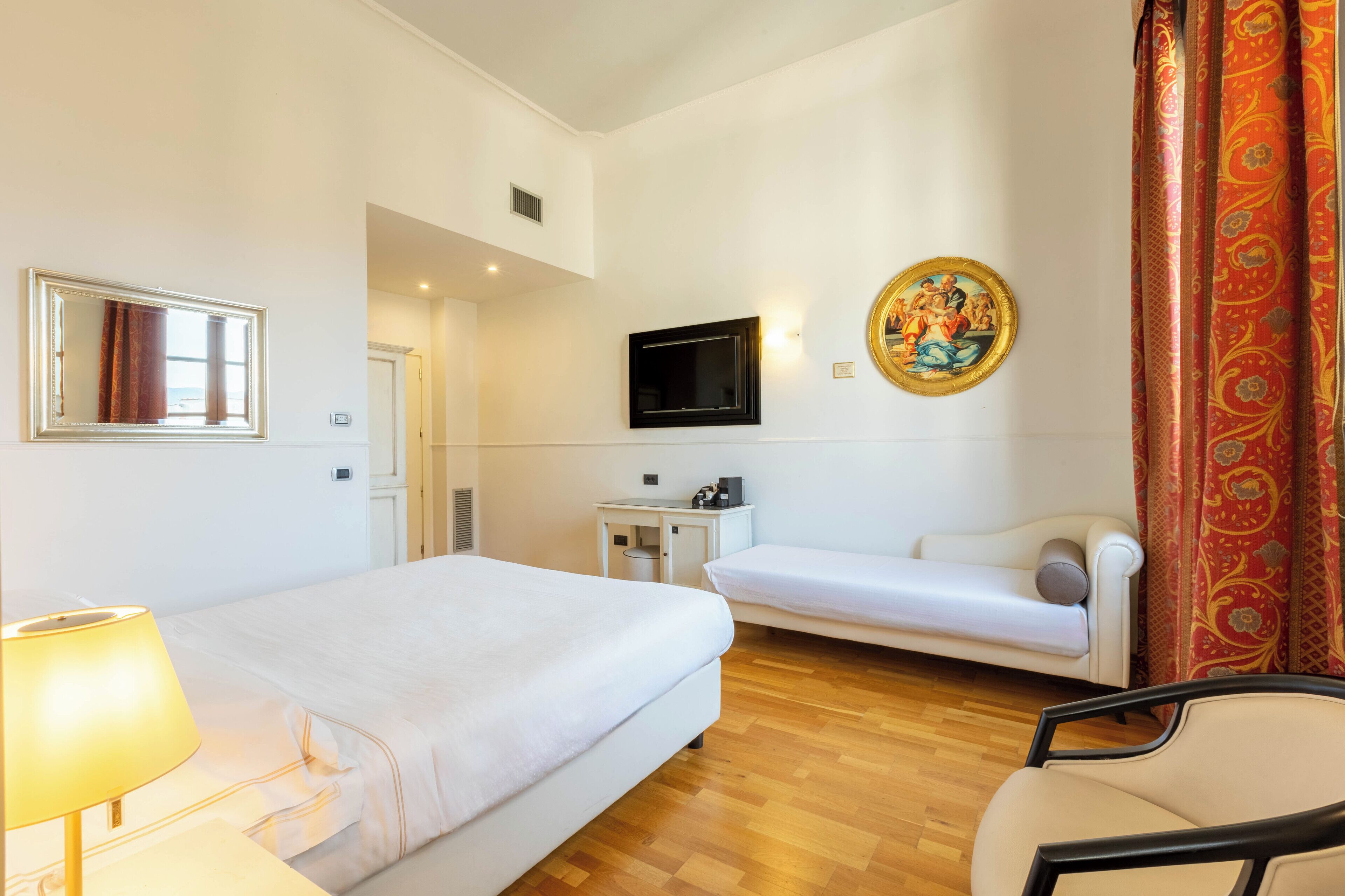 Una camera d'albergo con un letto, una poltrona, una sedia, una TV e un quadro appeso al muro.