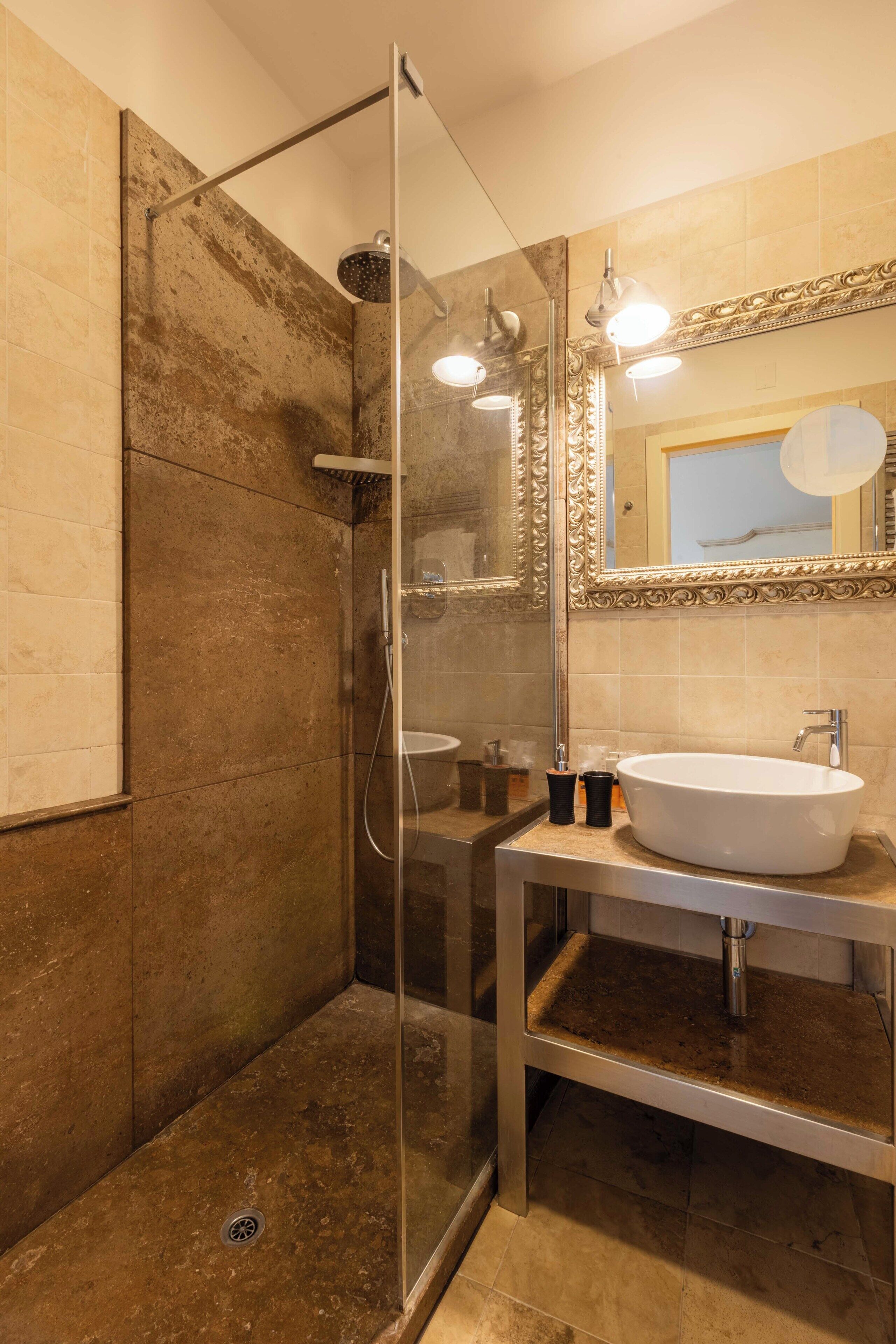 A modern bathroom with a glass-enclosed shower, a large mirror with ornate detailing, and a white sink.
