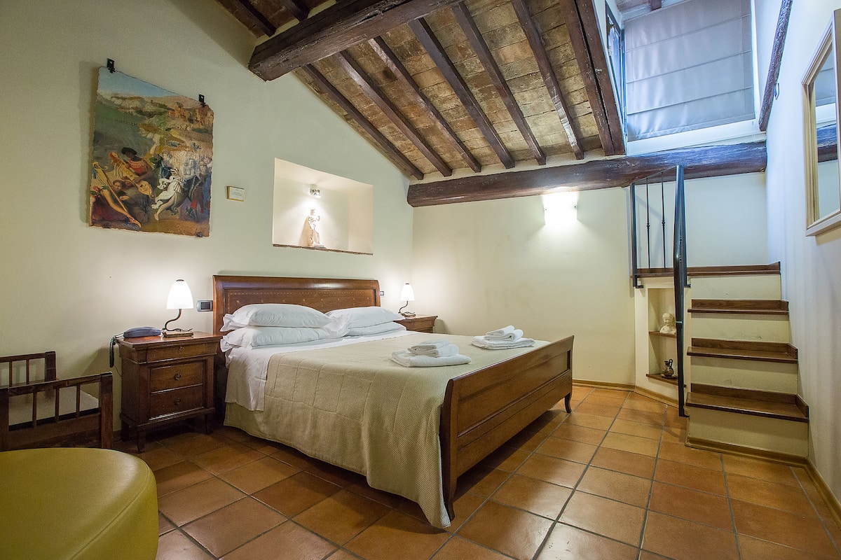 Een slaapkamer met een houten bed, een nachtkastje, een bedlampje, een schilderij aan de muur en een trap.