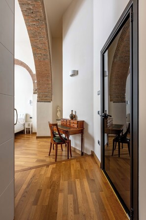 A room with a wooden floor, a dining table with chairs, a small white table, and a bed in the background.