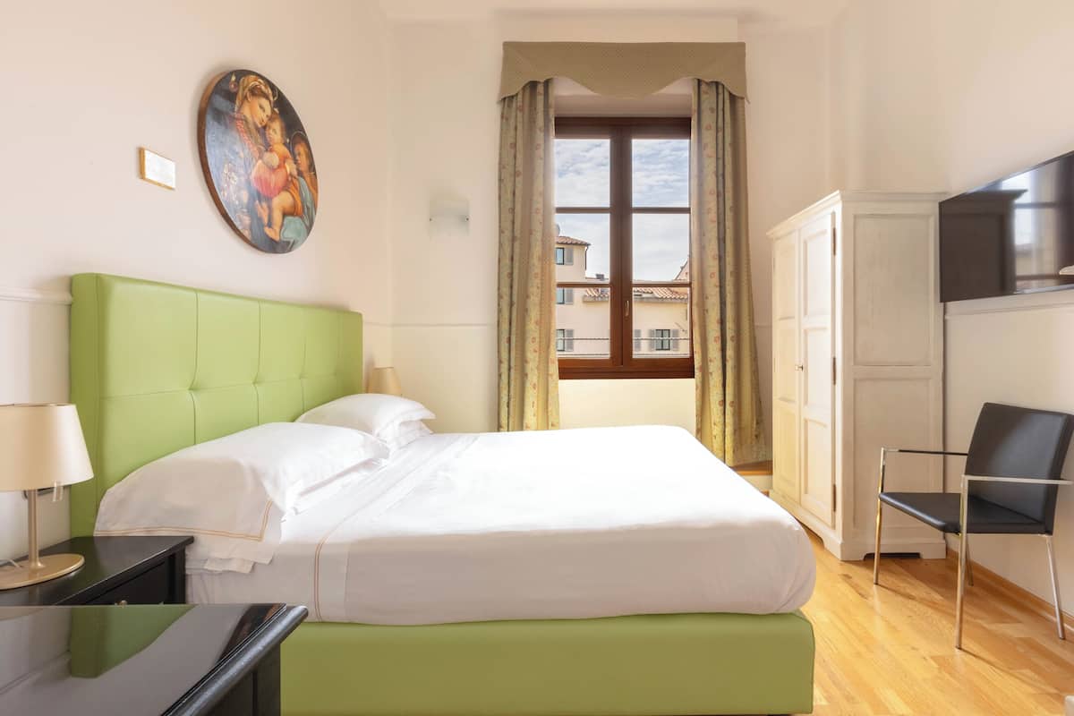 Hotelkamer met een groen bekleden bed, een flatscreen-tv, een bureau met een lamp en een schilderij aan de muur.