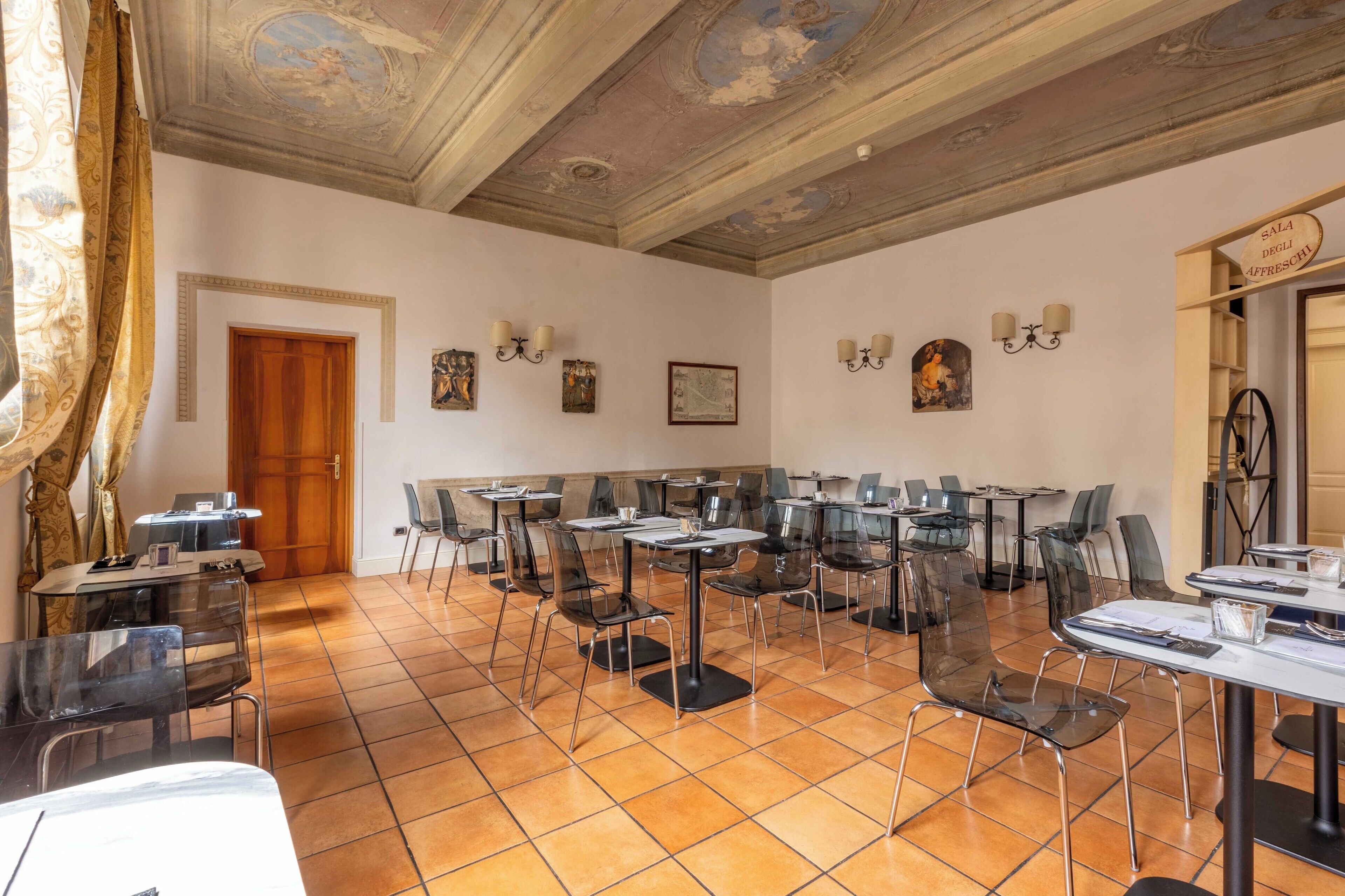 Zona pranzo con diversi tavoli e sedie, una porta in legno e opere d'arte appese al muro.