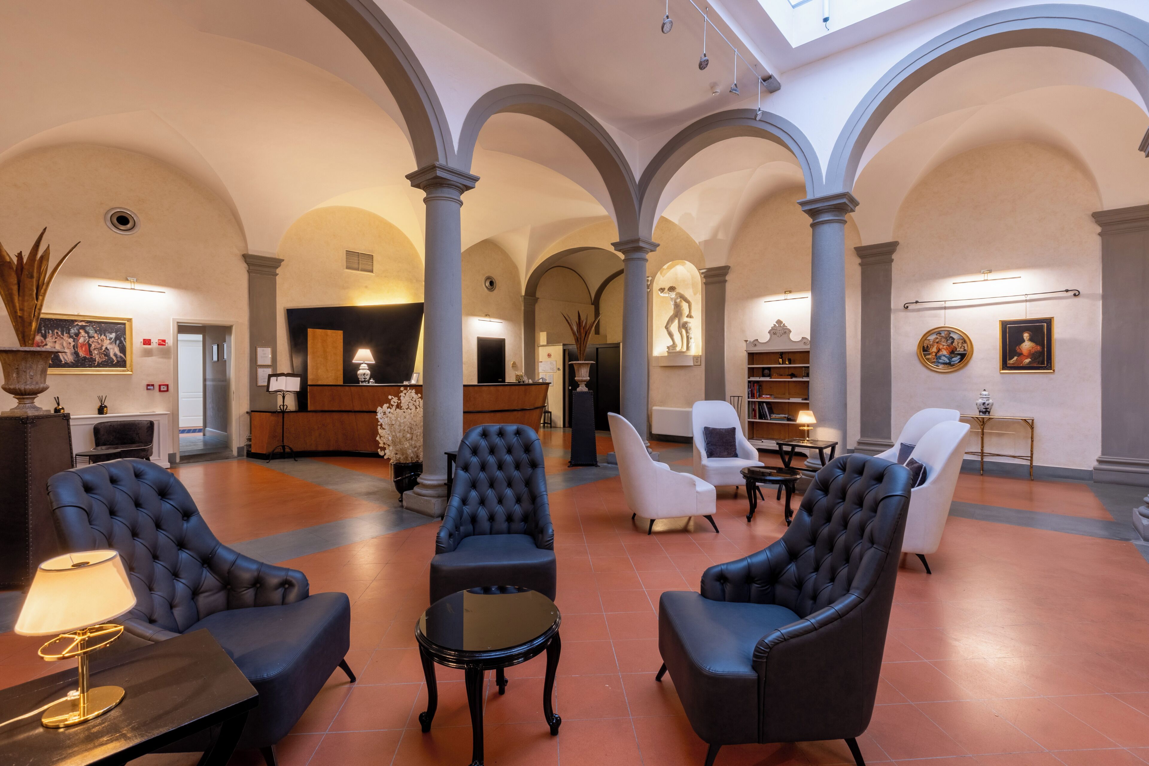 A spacious lobby with a high ceiling, arched columns, and a central seating area with upholstered chairs and a small table.