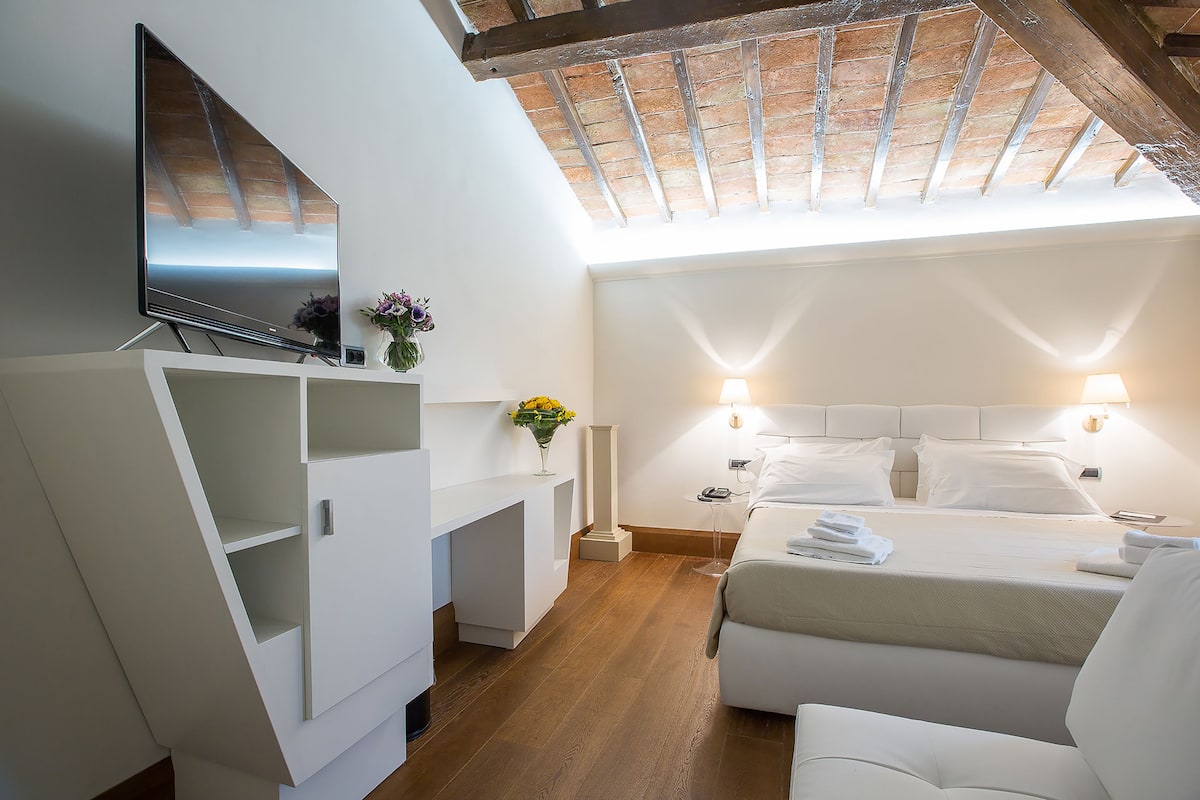 Een moderne hotelkamer met een groot bed, een televisie bevestigd aan een wit kastje, een bureau en een dakraam erboven.
