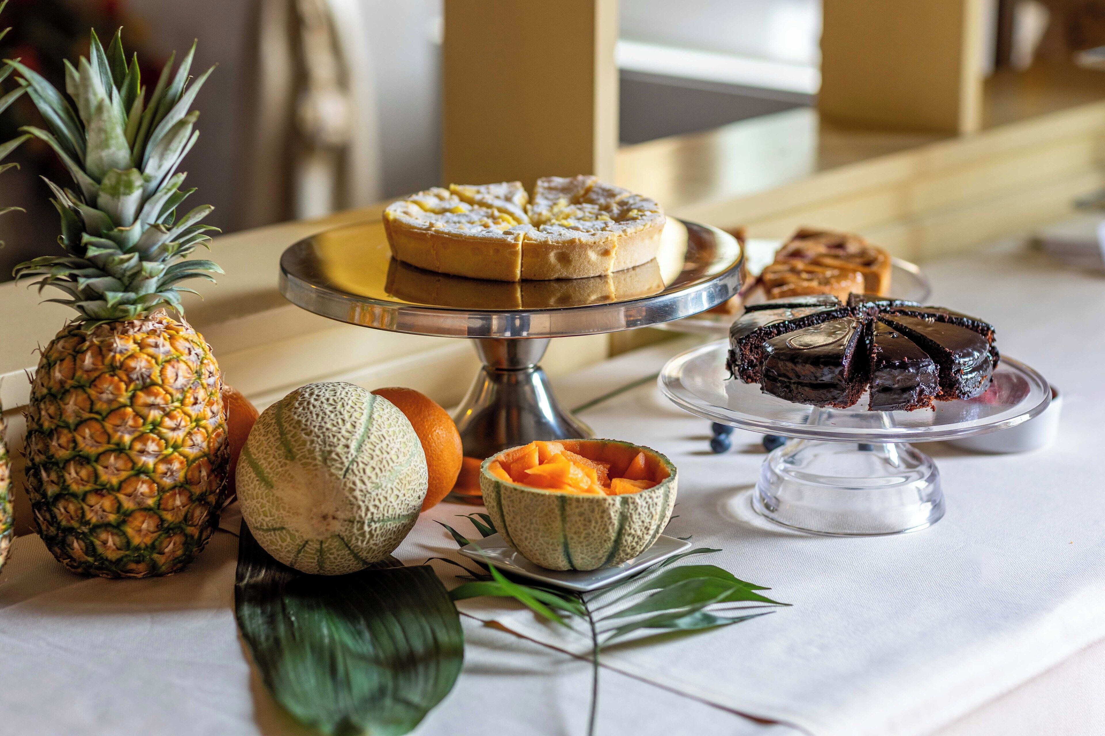 Ein Tisch mit verschiedenen Speisen, darunter eine Ananas, Melone und Desserts auf einem Tablett.
