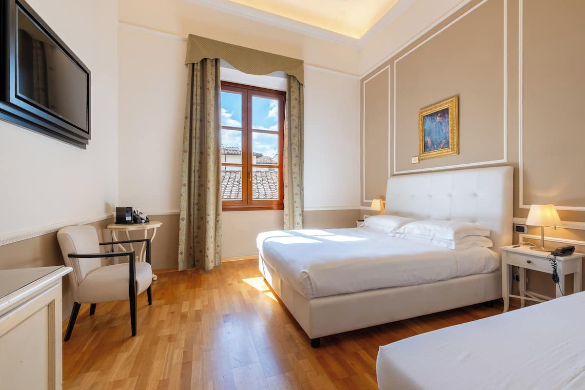 Een hotelkamer met een bed, een bureau, een stoel, een televisie en een raam met gordijnen.
