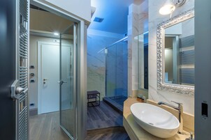 A modern bathroom with a glass shower, a marble wall, and a large mirror with an ornate frame.