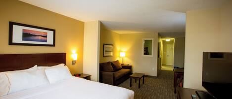 A hotel room with a large bed, a sofa, a desk, and a TV.