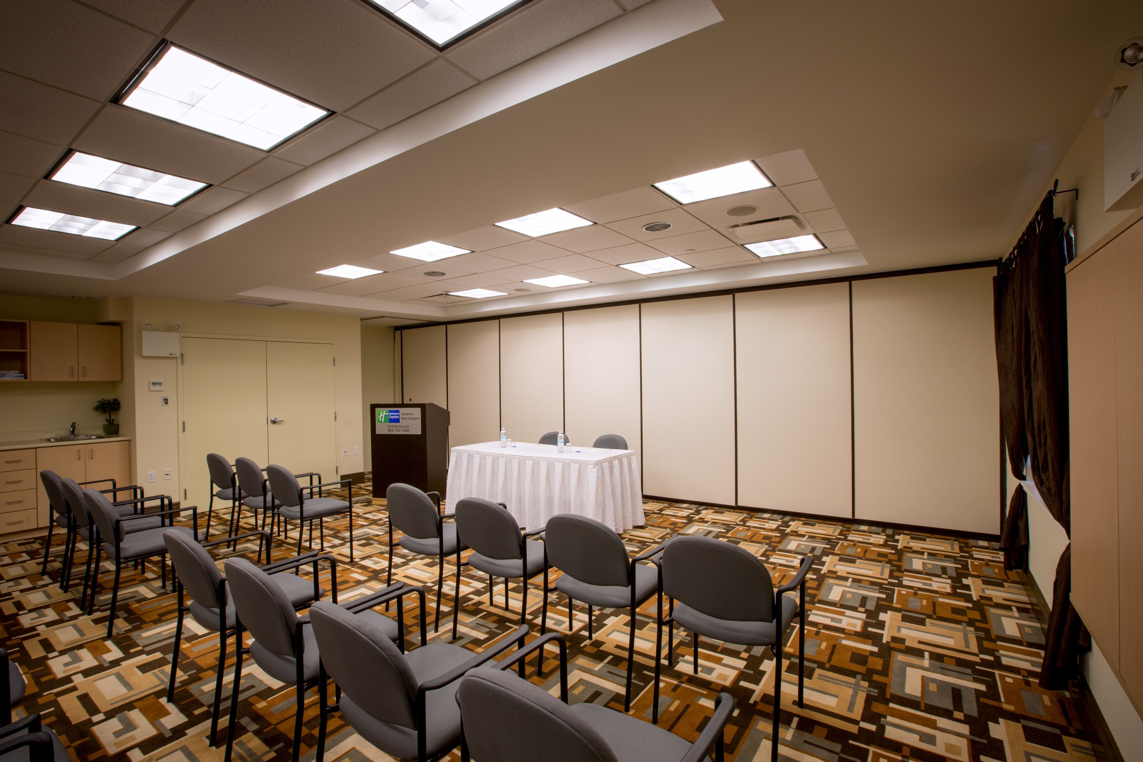 Une salle de conférence avec une table blanche, des chaises et un écran de projection.