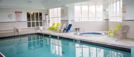 Una piscina interior con agua cristalina, rodeada de paredes y ventanas blancas. Se observan sillones de descanso y una zona de hidromasaje.