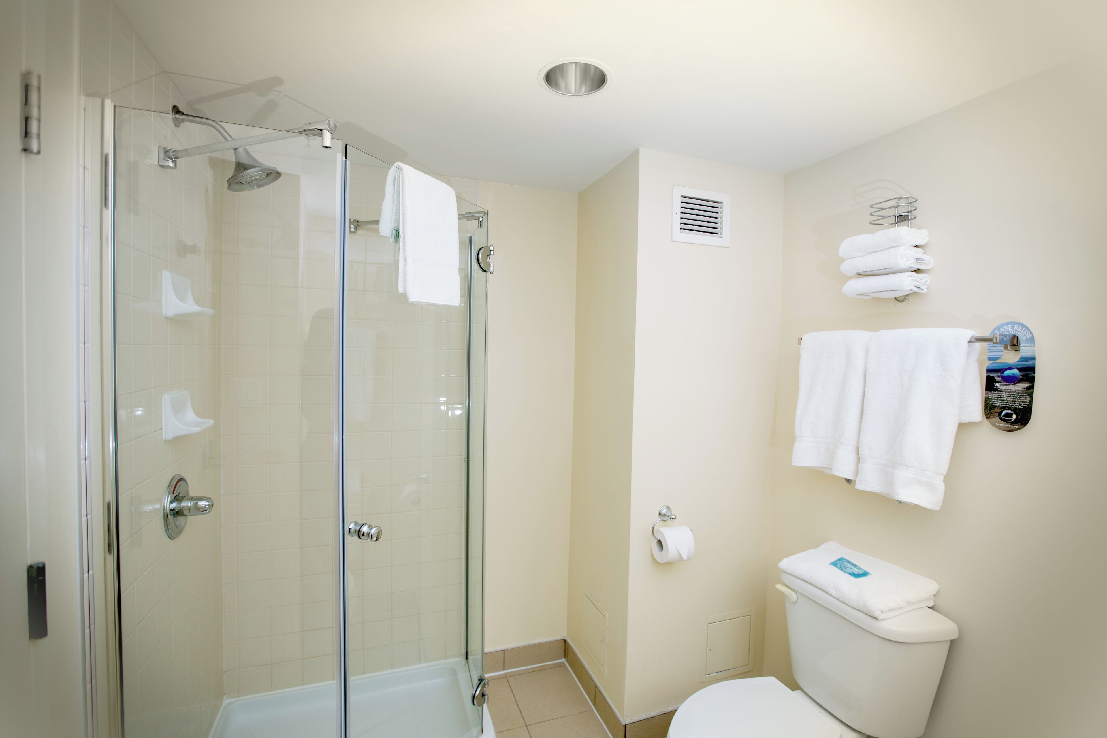 A bathroom with a glass-enclosed shower, a toilet, and a towel rack with multiple towels.