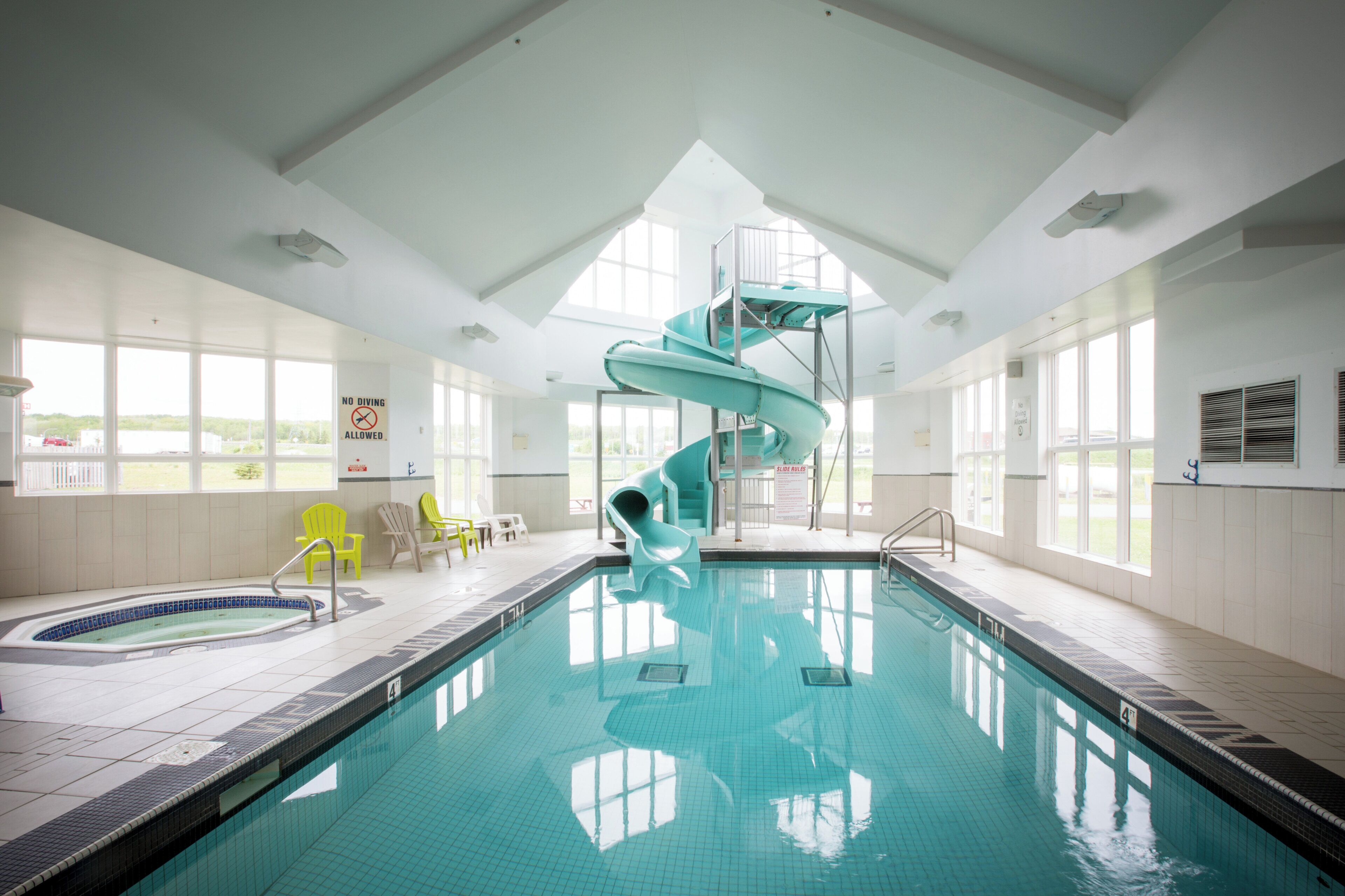 An indoor swimming pool with a spiral slide, clear pool tiles, and a view of the outdoors through large windows.