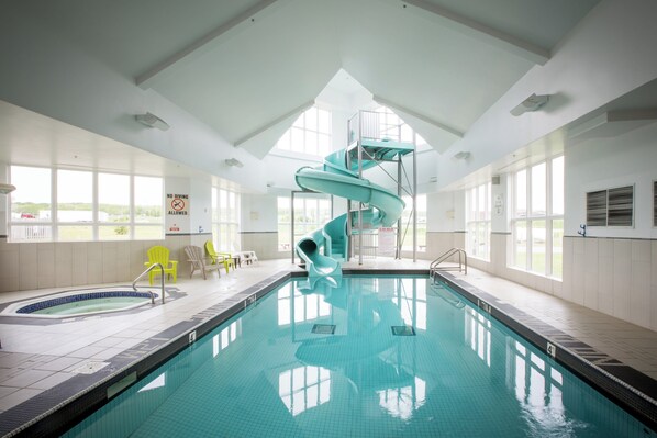 Una piscina interior con un tobogán en espiral, azulejos de piscina brillantes y vistas al exterior a través de amplios ventanales.