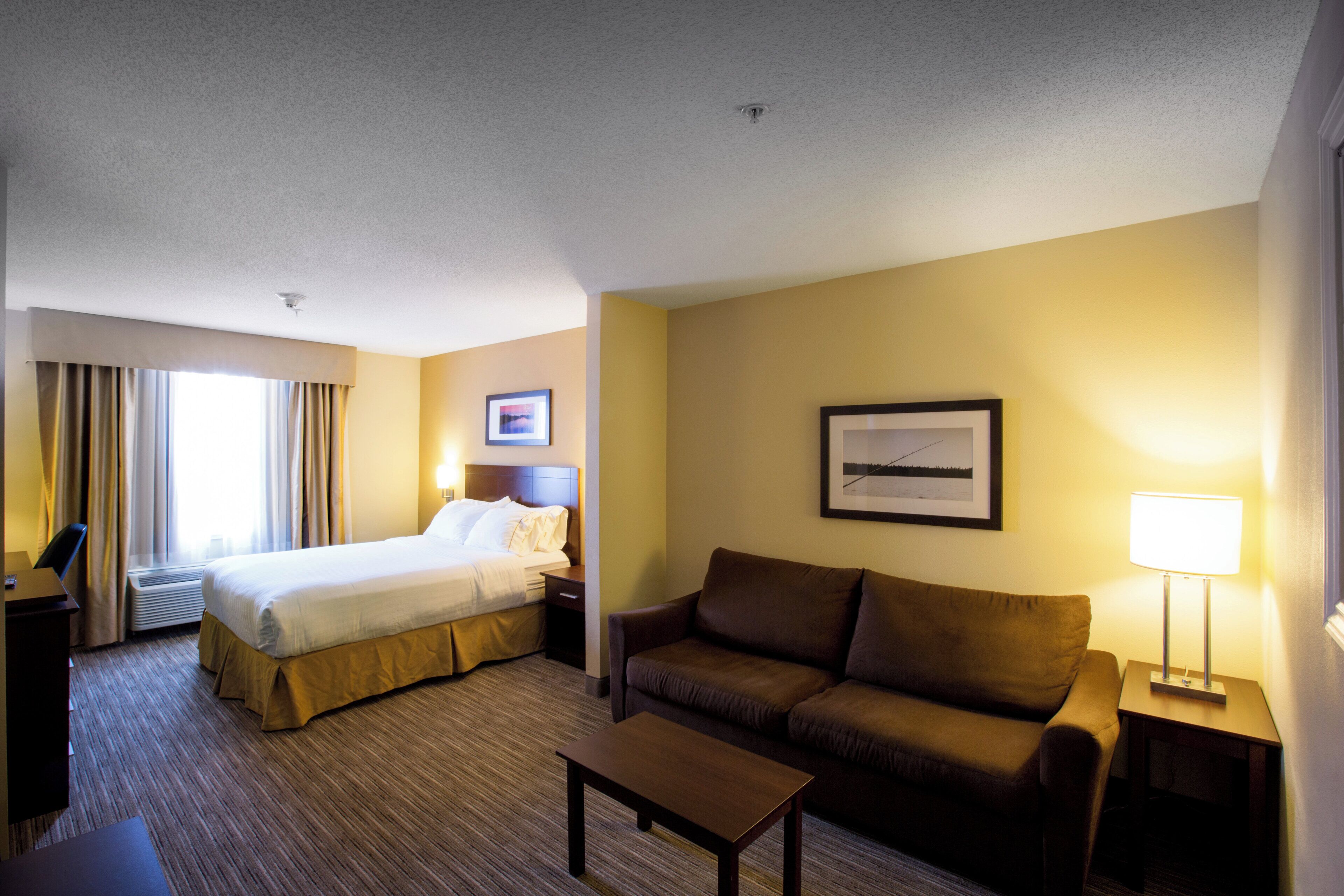 A hotel room with a bed, a sofa, a desk, and a lamp.