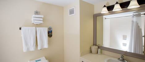 A bathroom with a toilet, sink, and mirror. There are towels hanging on the wall and a shower curtain visible in the mirror.