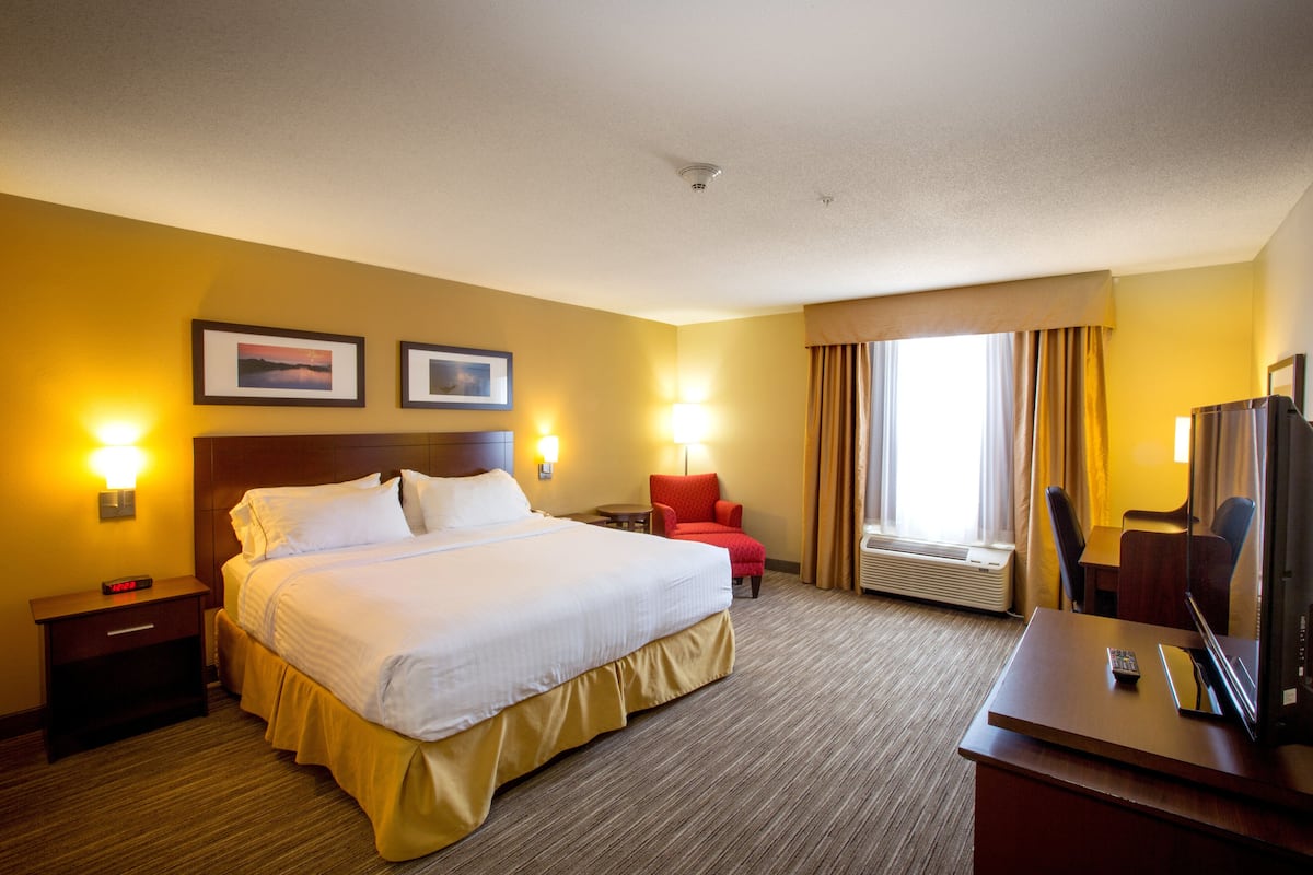A hotel room with a large bed, bedside tables, a desk with a chair, a TV, and a window with curtains.