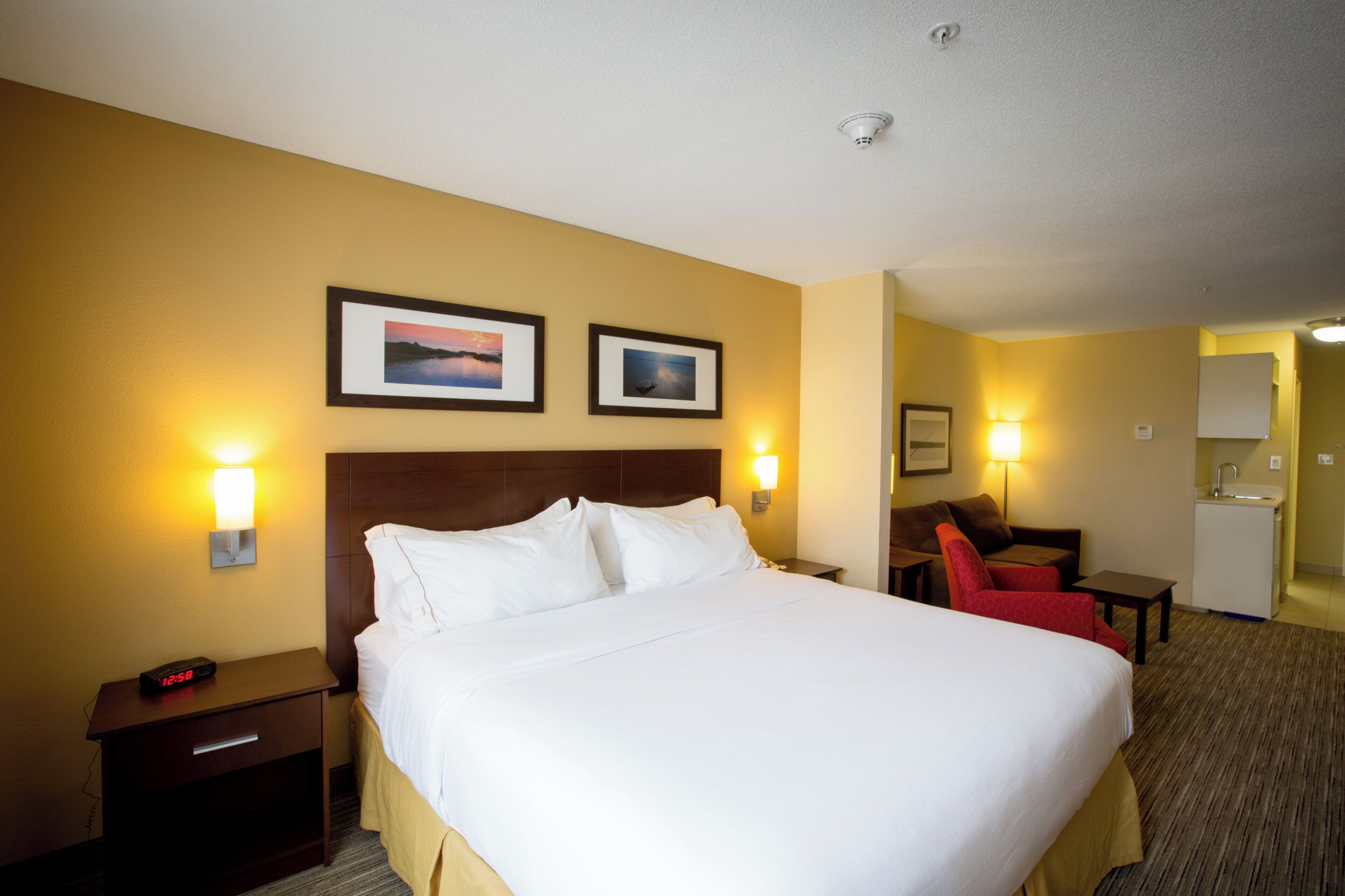 A hotel room with a bed, bedside tables, a desk, a chair, and two framed pictures on the wall.