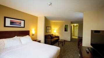 Ein Hotelzimmer mit einem großen Bett, einem Schreibtisch, einem Sessel, einer Couch und einem Fernseher.