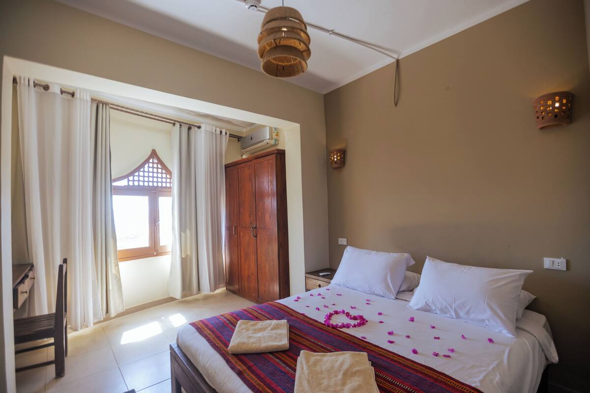 Une chambre d’hôtel avec un lit, un bureau et une vue sur un bâtiment traditionnel, visible par la fenêtre.