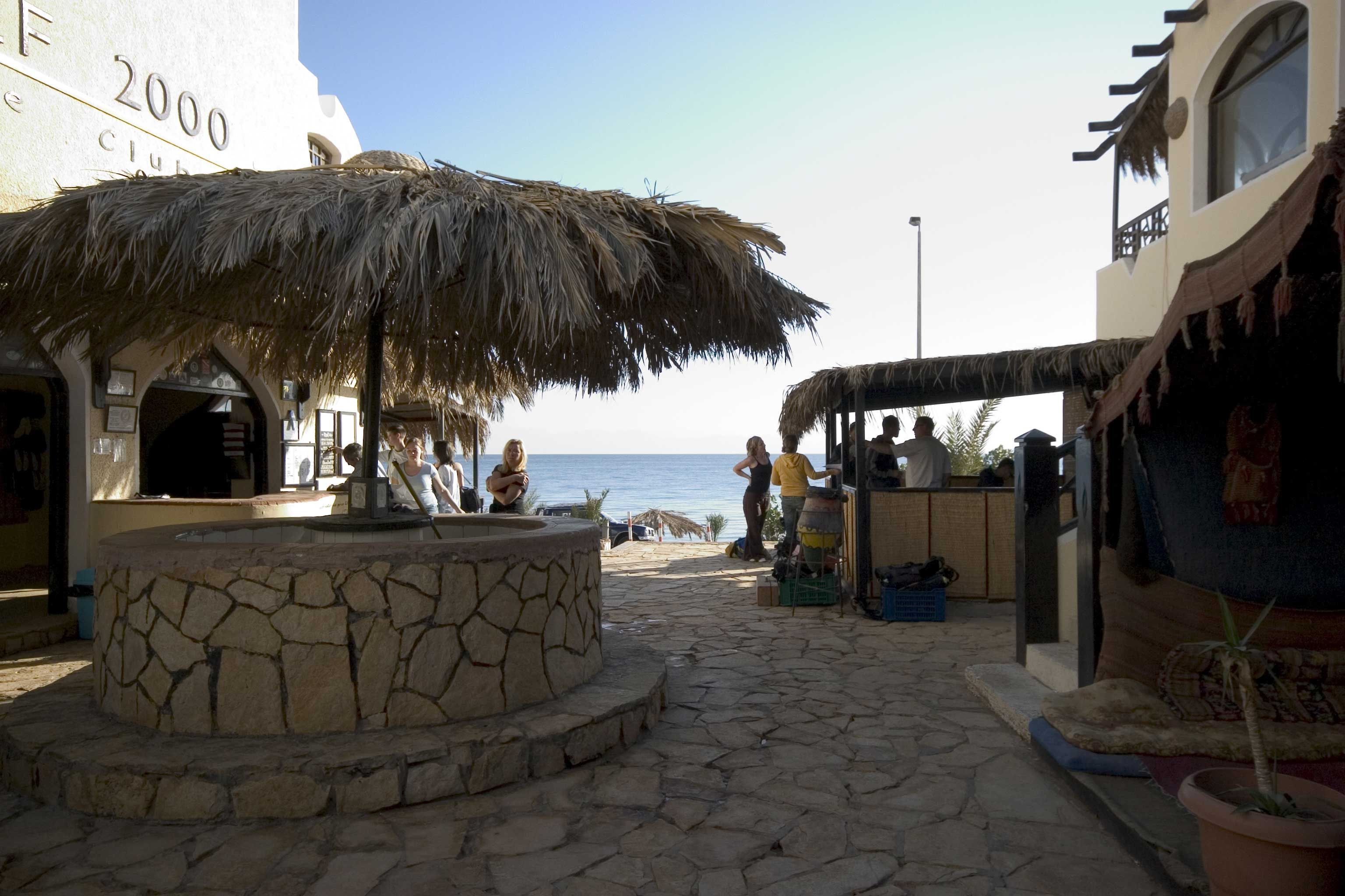 A stone-paved area with a thatched umbrella, a stone fountain, and a beach view.