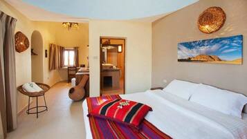 A hotel room with a bed, a small stool, a chair, a mirror, and a painting on the wall.
