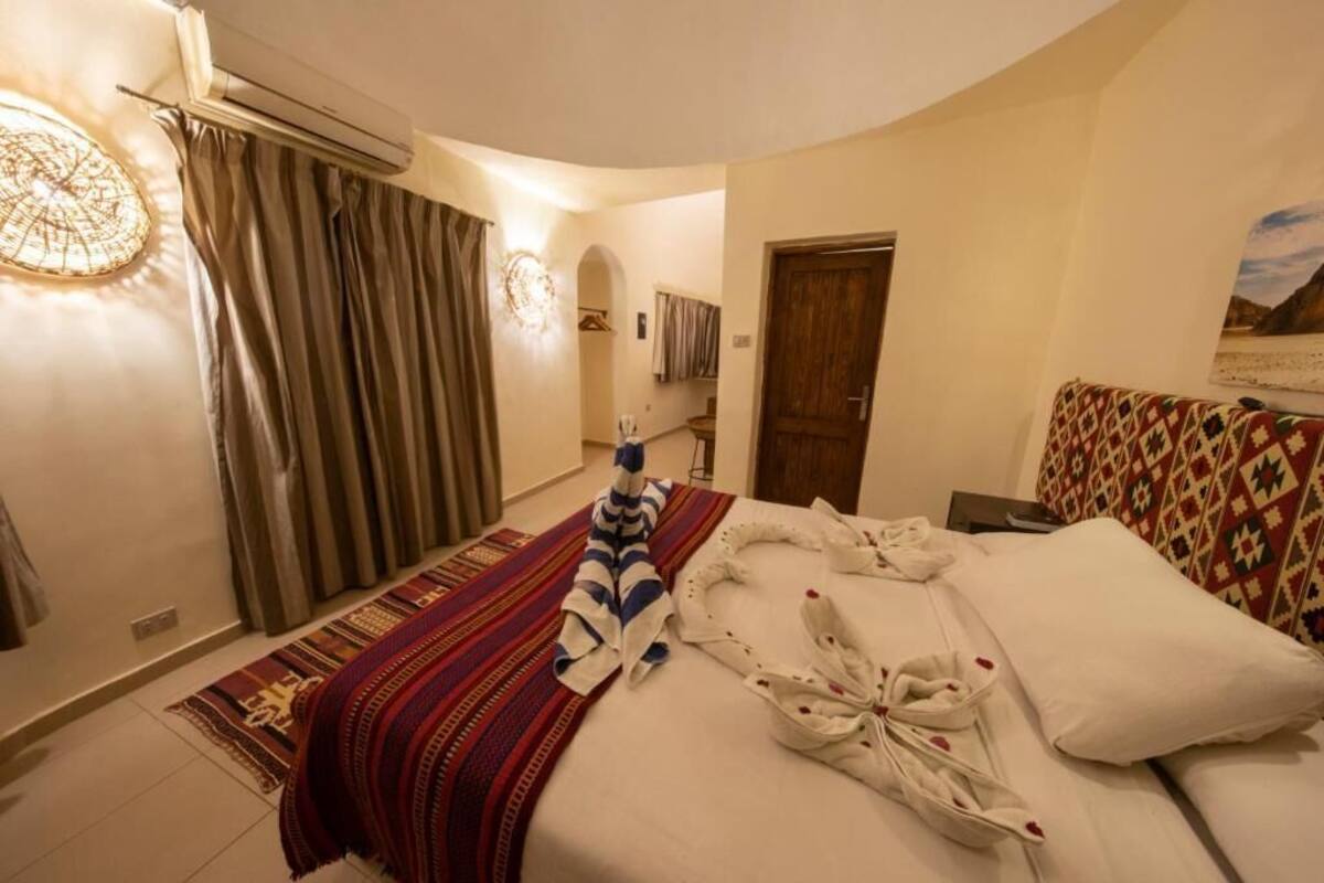 Une chambre d’hôtel avec un lit, un tapis à motifs, un luminaire fixé au mur et une porte.
