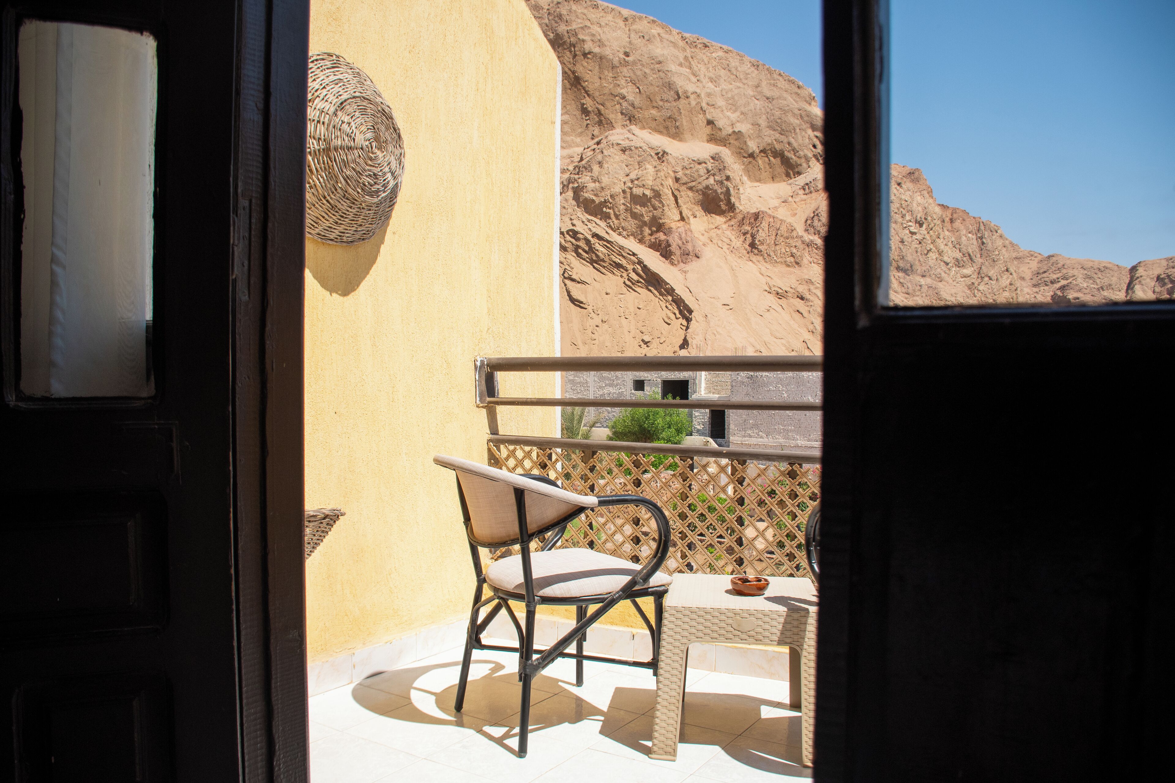 Un balcon avec un fauteuil en osier et une petite table, donnant sur un paysage montagneux.