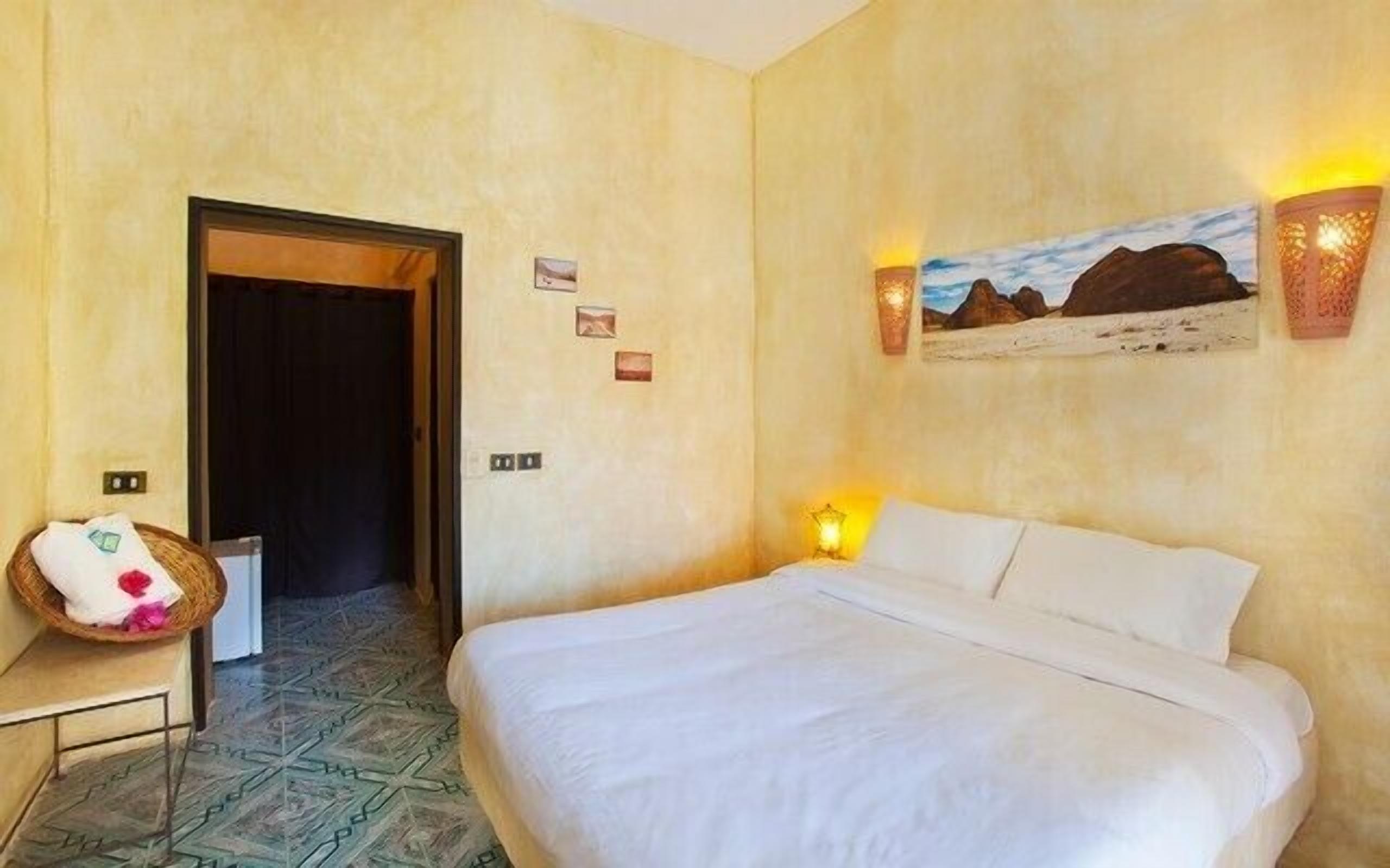 A hotel room with a bed, a wall-mounted lamp, a painting, and a door.