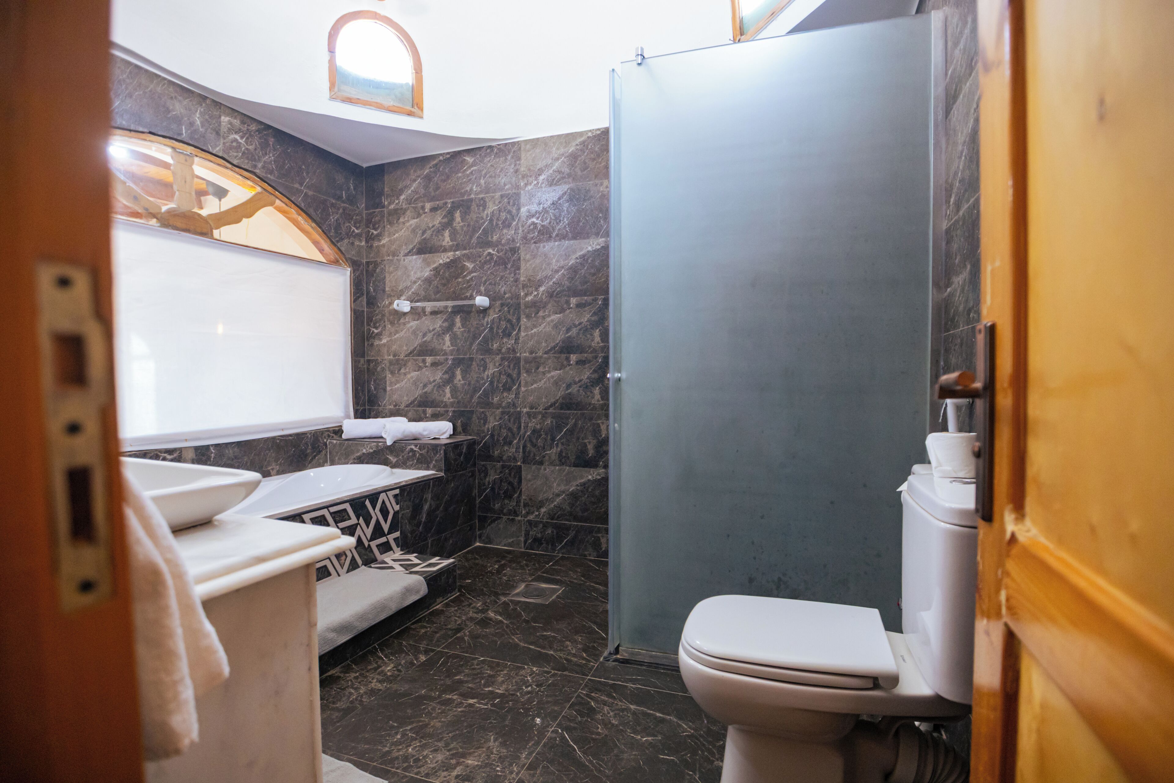 Ein modernes Badezimmer mit Marmorwand, Toilette, Waschbecken und Duschbereich.