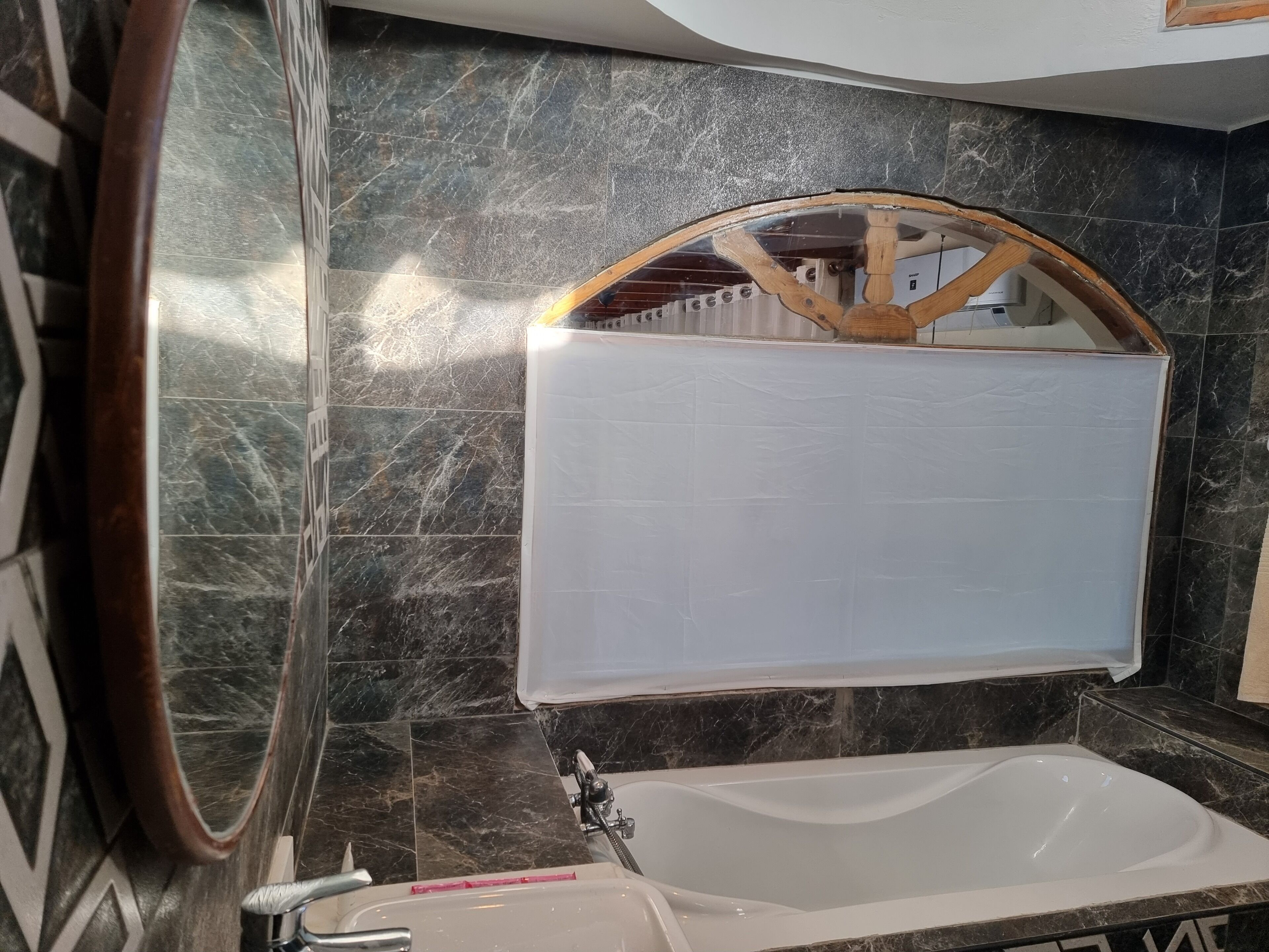 Ein Badezimmer mit einer weißen Badewanne, einem spiegelnden Holzrahmen und dunklen Marmorfliesen.