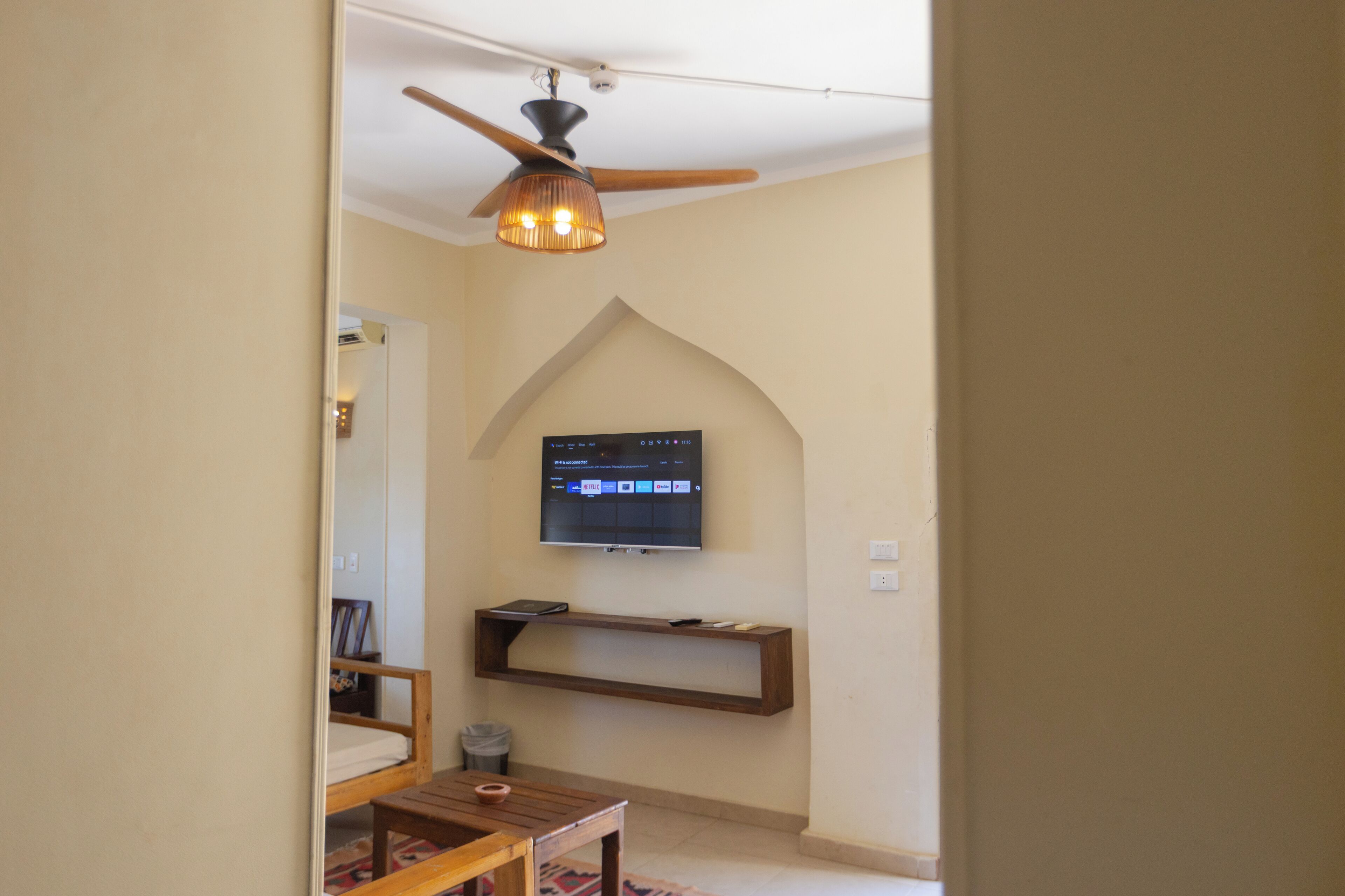 Ein Wohnzimmer mit Deckenventilator, einem Wand-Fernseher, einem Holzregal und einem kleinen Tisch.