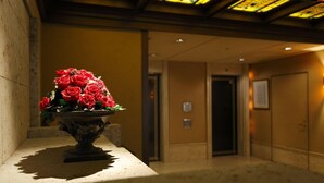 Un espace d’accueil avec un vase de roses rouges posé sur une table sur pied, un comptoir d’accueil et un couloir menant à une porte.