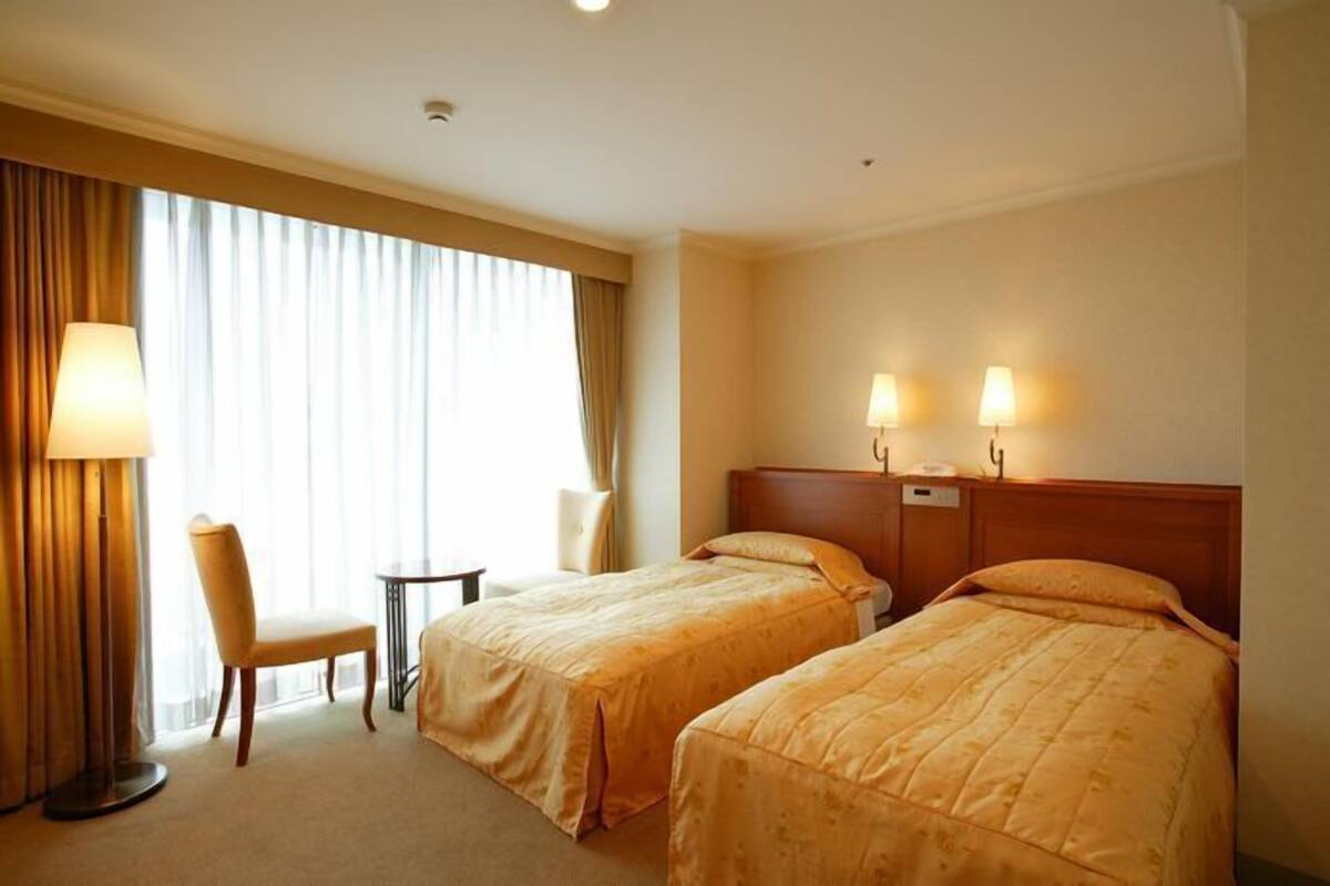 Una habitación de hotel con dos camas, una silla, una mesita y una lámpara.