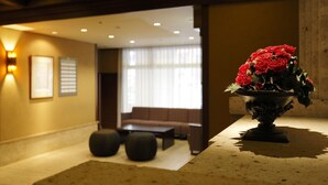 Un hall d’entrée avec un canapé, une table basse et un vase décoratif orné de fleurs rouges.