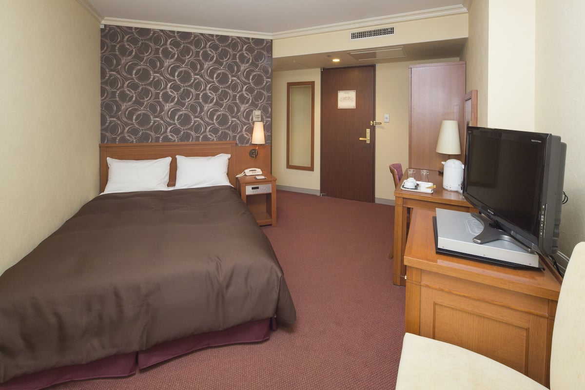 Habitación de hotel con una cama grande, un escritorio con televisor, teléfono y una puerta que da a otra habitación.