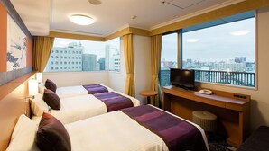 Une chambre d’hôtel avec deux lits, un bureau avec une télévision et une vue sur la ville.