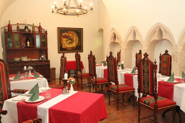 A dining hall with red tablecloths, wooden chairs, and a chandelier.
