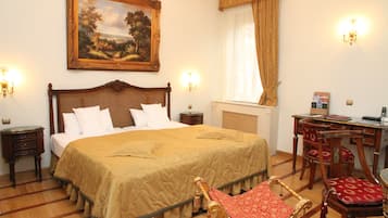 A hotel room with a large bed, a desk with a chair, a painting on the wall, and a chandelier.