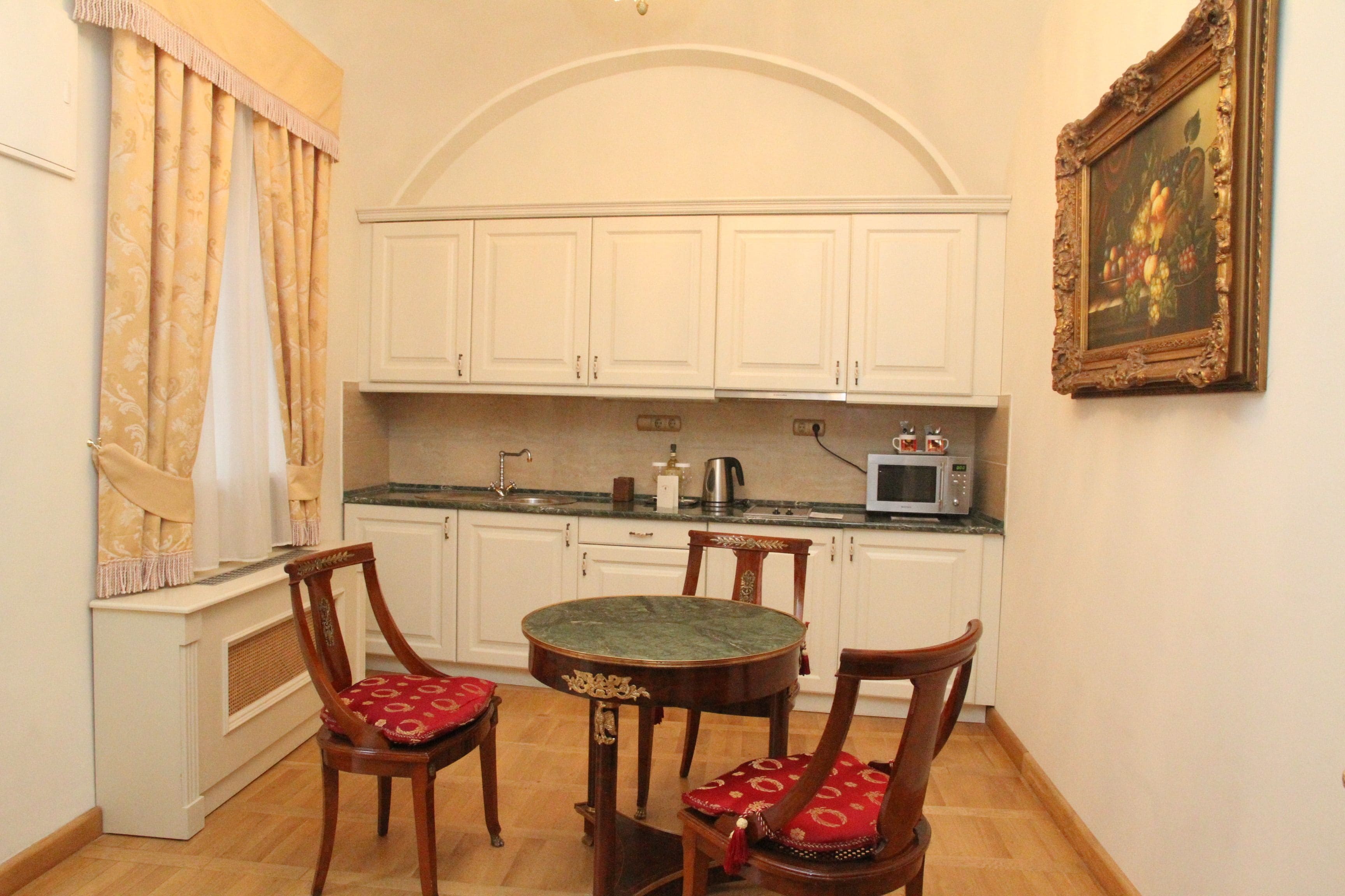 A compact kitchen with white cabinets, a microwave, and a dining table with chairs.