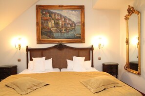 A hotel room with a large bed, two bedside tables, a painting of a coastal scene, and a large mirror. - St. George Residence All Suite Hotel Deluxe (Budapest)