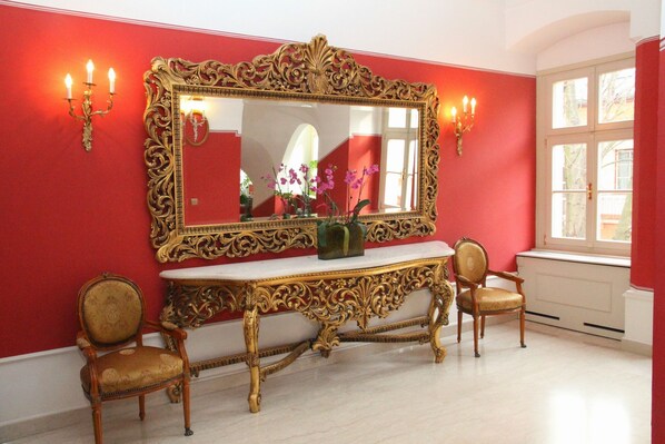 A room with a large ornate mirror, two chairs, a white console table, and a window with a view.