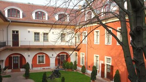 A courtyard with a brick pathway, potted plants, and a cannon. - St. George Residence All Suite Hotel Deluxe (Budapest)