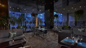 An outdoor seating area with tables and chairs, potted plants, and a view of buildings. - Hilton Garden Inn Montréal Centre-ville (Montreal)