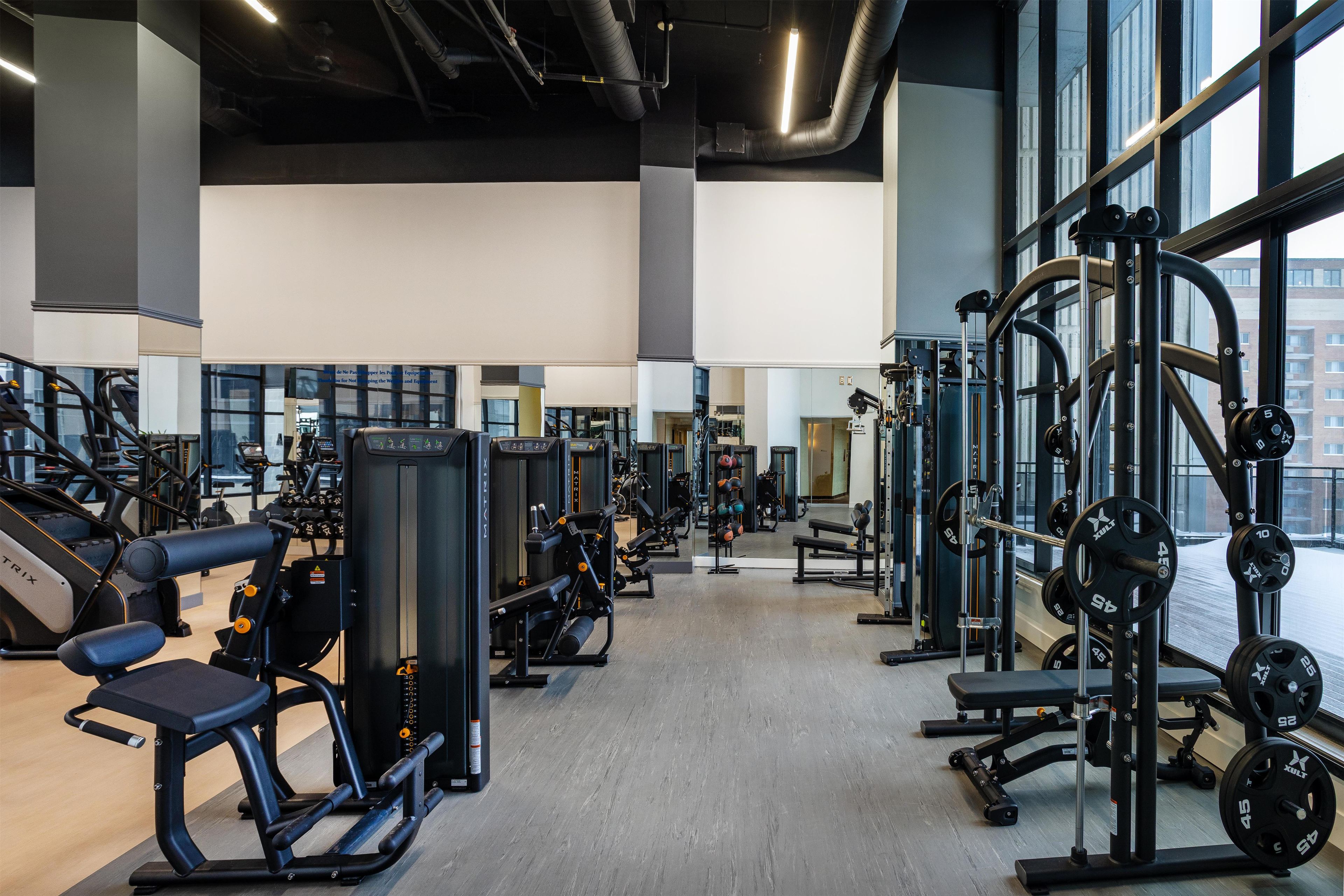 A gym with various exercise equipment, large windows, and a high ceiling.