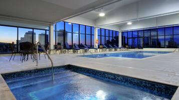 Piscina con sillones de descanso y vista a la ciudad al anochecer.