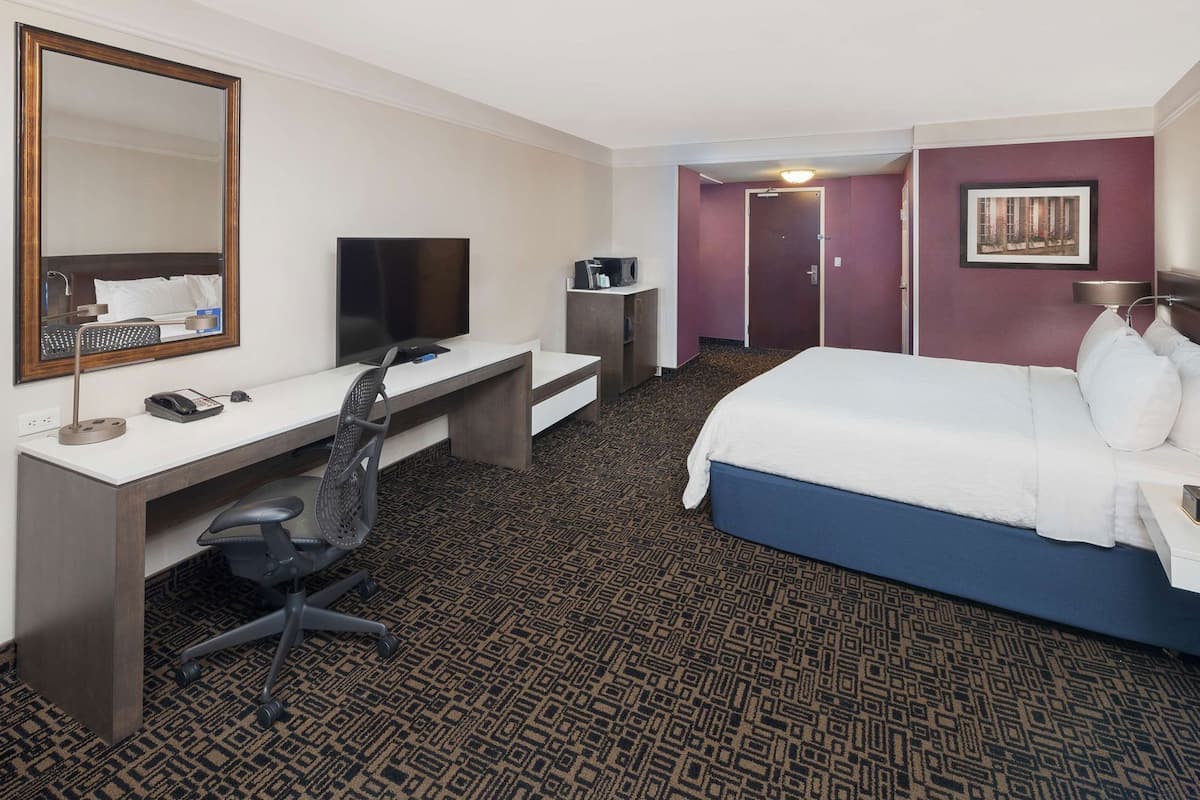 Une chambre d’hôtel équipée d’un lit, d’un bureau, d’une chaise, d’une télévision et d’un miroir.